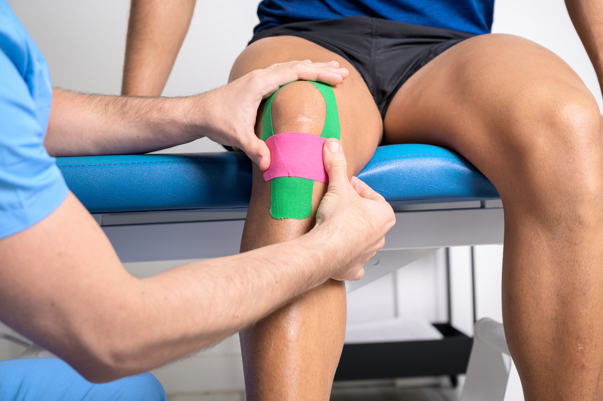 Physical Therapist Applying Kinesio Tape on Male Patient Knee. Kinesiology, Physical , Rehabilitation Concept. Close up